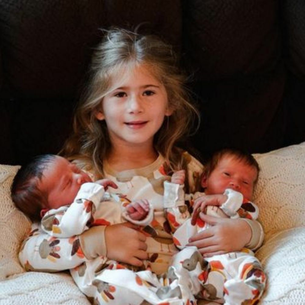 sister holding newborn twin siblings